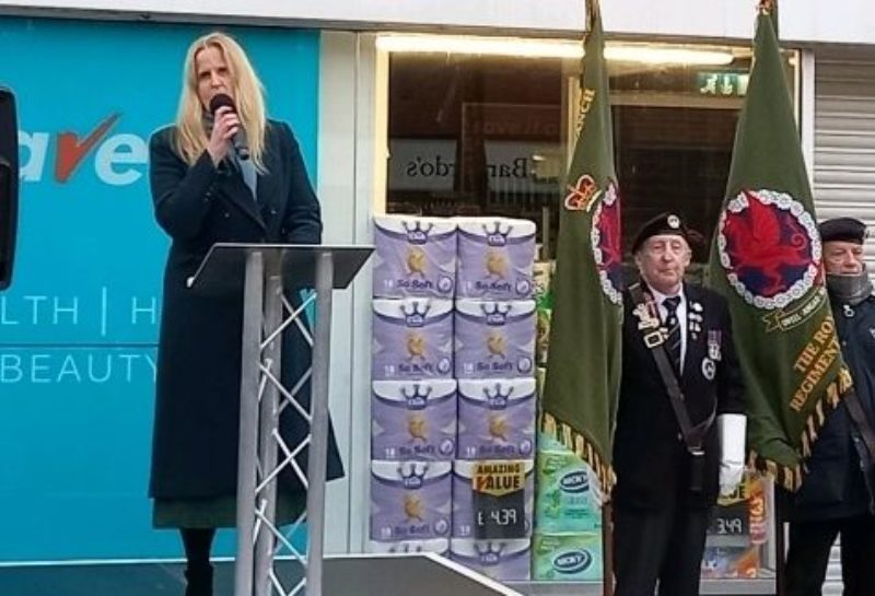 Image of Beth Winter speaking on platform with veterans behind.